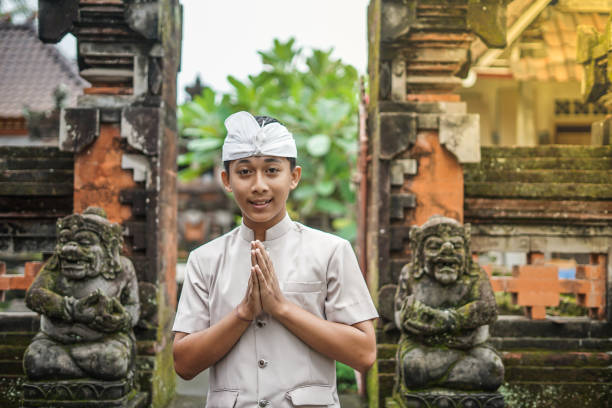Denpasar, Bali island, Indonesia - June 23, 2018: Young men dressed in ethnic Balinese people costumes with traditional umbrellas tedung before ritual temple procession at street of Denpasar