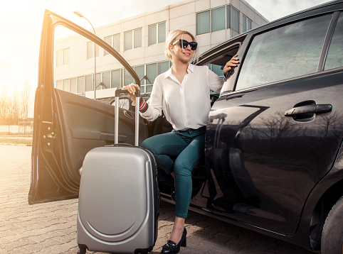 Attractive young businesswoman with luggage getting out of the car