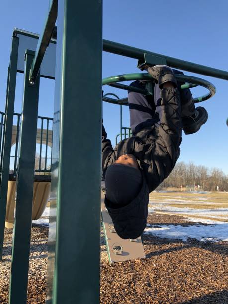 A young boy plays on playground equipment on a bright sunny early spring day A young boy of African descent plays on playground equipment on a bright sunny early spring day. He is playing on the monkey bars black hat upside down stock pictures, royalty-free photos & images