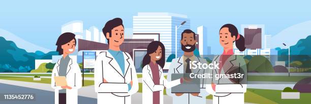 Group Of Mix Race Doctors Team In Uniform Standing Together Over Hospital Building Modern Medical Clinic Exterior Cityscape Background Portrait Flat Horizontal Stock Illustration - Download Image Now