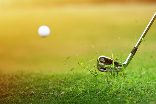 Close-up of golf ball hitting hard flying from the grass.