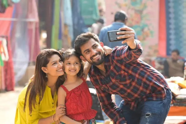 Happy Indian family taking selfie using mobile camera at street market