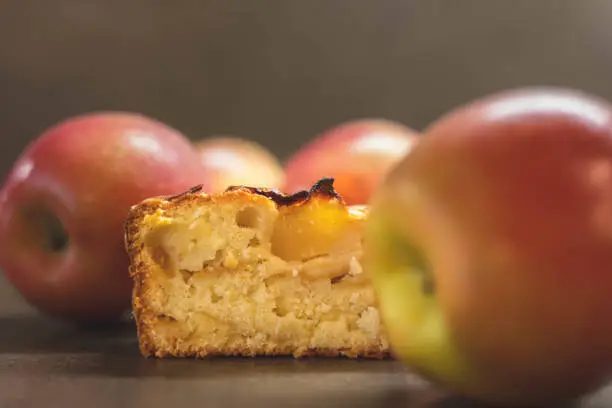 Closeup of an apple cake slice surrounded by fresh apples