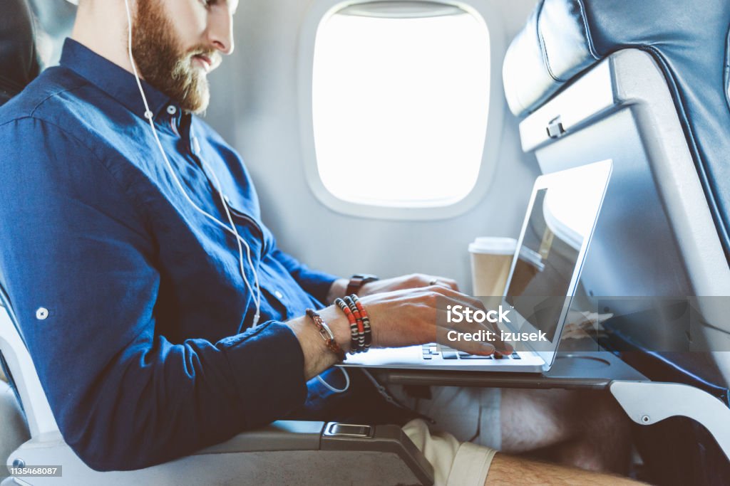 Man using laptop in airplane Side view of a male traveler in a flight using laptop computer. Man using laptop during his journey by airplane. Airport Stock Photo