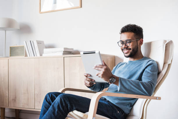 веселый человек, использующий цифровой планшет в домашних условиях - reading business one young man only working at home стоковые фото и изображения