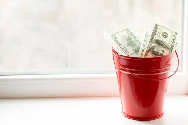 Dollar bills in red pail. on white window.light background. place for text. top view. a lot of money