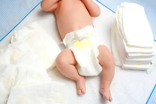 Feet of newborn baby on changing table with diapers. Cute little girl or boy two weeks old. Dry and healthy body and skin concept. Baby nursery