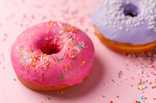 Concept of cooking, baking and food - close-up. Two donuts in pink and violet glaze on a pink background. Trend colors. Appetizing still life.