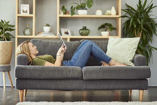 Full length shot of an attractive young woman using her tablet while relaxing on the sofa at home