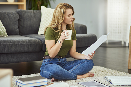 Full length shot of an attractive young woman looking over her home finances while sitting on the floor at home