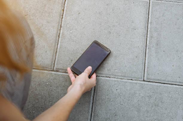istock Woman is picking up broken smartphone lying on the road outdoors. Crashed screen from the accidental fall. Fragile modern technologies. 1135476237