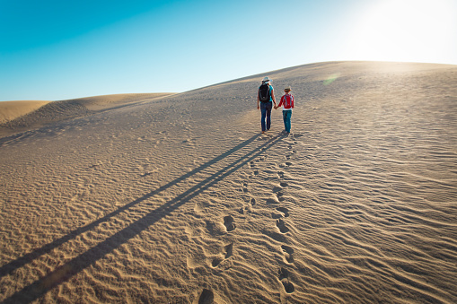 mother and son walk in sand dunes, leaving footprints in sand, travel concept