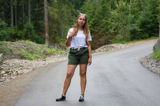 piękna dziewczyna stoi na środku górskiej drogi w białym t-shircie i szortach. - stripped shirt zdjęcia i obrazy z banku zdjęć