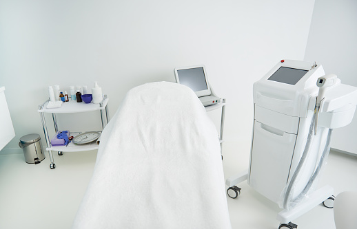 Laser hair removal machine and comfortable daybed covered with white sheets waiting for clients