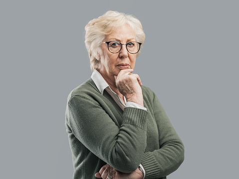 Pensive senior woman thinking with hand on chin, she is sad and concerned