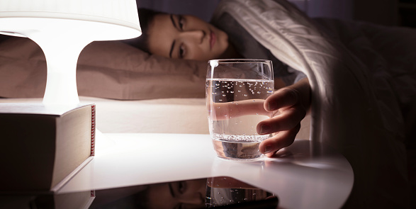 Woman drinking a glass of water before going to sleep, she is lying in bed