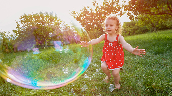 Cute little girl trying to catch soap bubbles while running in park.