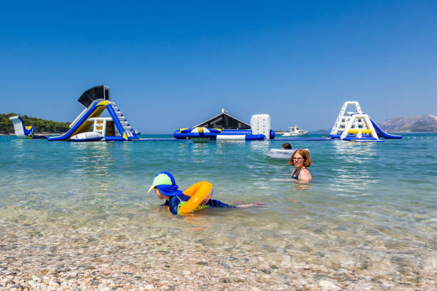 Mother and child swim and having fun in the water with inflatable slides in the background. stock photo