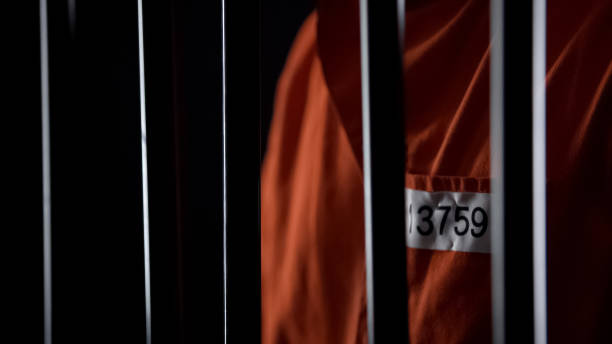 Prisoner in orange uniform standing behind bars, punishment for committed crime stock photo