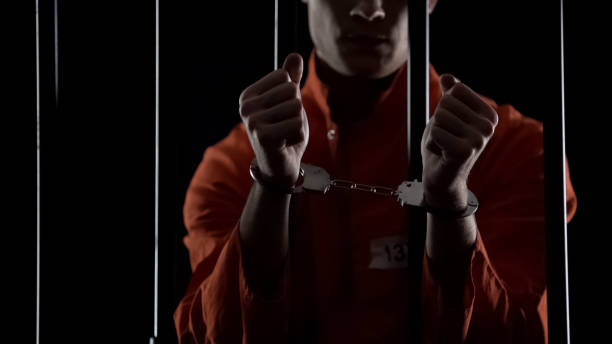 istock Prisoner in orange uniform showing handcuffs, looking angry and disappointed 1135489430