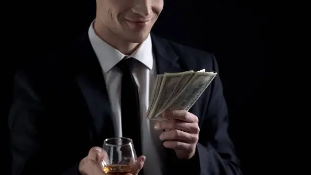 Businessman holding dollar cash and drinking cognac, celebrates income increase
