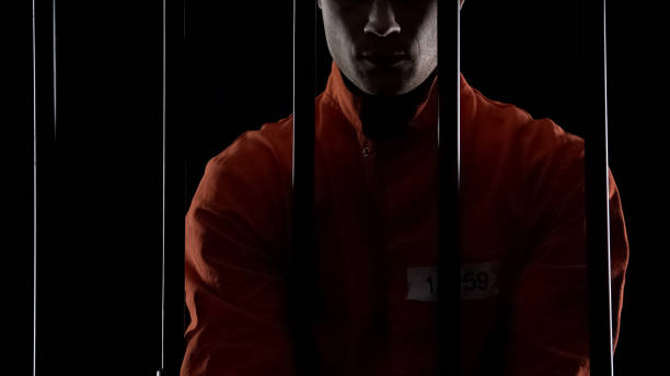 istock Prisoner in orange uniform standing behind bars, punishment for committed crime 1135489664