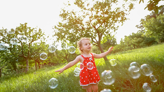 Cute little girl playing with soap bubbles in park.