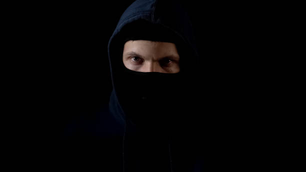 istock Hooded serious criminal in balaclava looking at camera, piercing glance, concept 1135490682