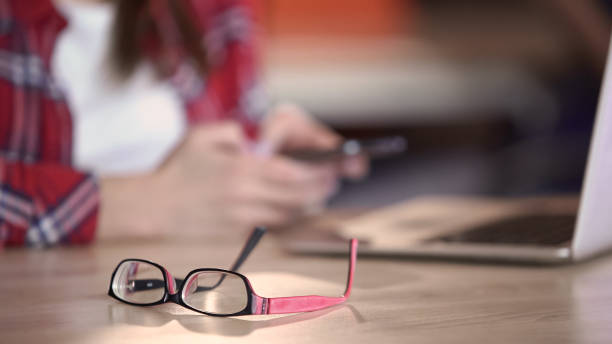 istock Stylish eyeglasses lying on table, woman texting on smartphone, communication 1135490746