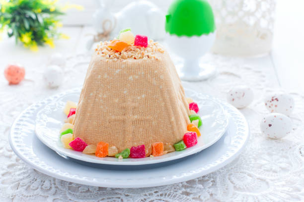 Traditional cottage cheese Easter with nuts and candied fruits on a white table with white Easter bunnies, festive food, horizontal