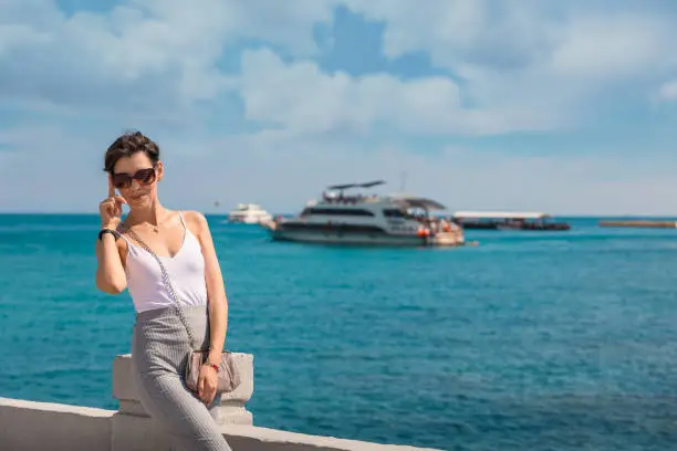 Photo of Cheerful and beautiful girl resting fun in vacation, on the pier on background of boat. In China, Hainan city of Sanya. View of island in bay. Town Sanya is popular tourist destination in China