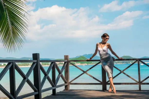 Photo of Cheerful and beautiful girl resting fun in vacation, on the pier on background of city. In China, Hainan city of Sanya. View of island in bay. Town Sanya is popular tourist destination in China