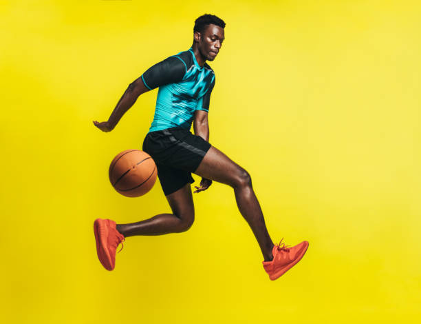 Basketball player in action Young basketball player dribbling a ball over yellow background. Man in sportswear practicing basketball. professional sportsperson stock pictures, royalty-free photos & images