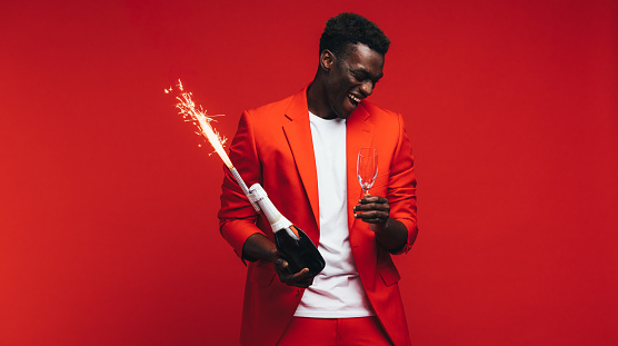 African man celebrating new years with champagne and firework. Stylish guy having fun against red background.