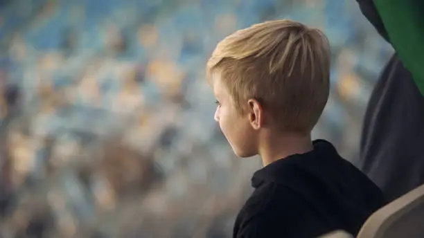Little boy watching sport game at stadium, supporting favorite team, close-up