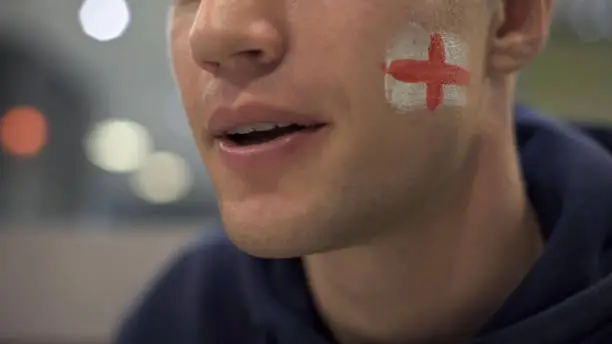 Football fan with English flag painted on cheek watching match enthusiastically