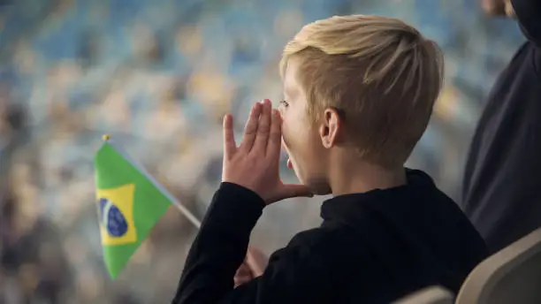 Little boy with Brazilian flag chanting at stadium in support of football team