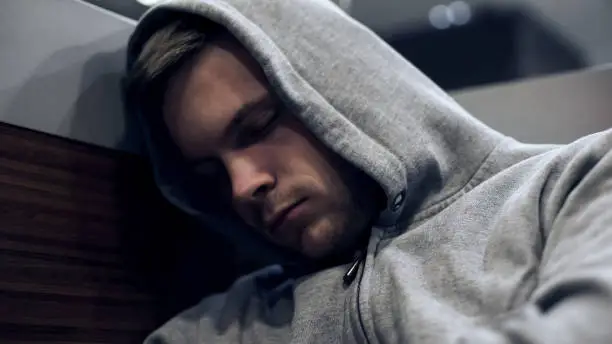 Homeless man in hoodie sleeping in public transport, unemployment problems