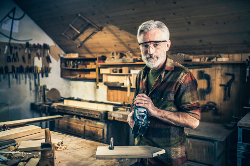 Portrait of a senior woodworker holding an electric saw and looking at the camera.