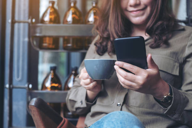 カフェでコーヒーを飲みながらスマートフォンを使って見ている美しいアジア人女性のクローズアップ画像