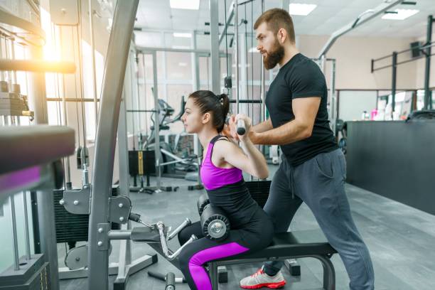 personal fitness trainer coaching and helping client woman making exercise in gym. sport, teamwork, training, people concept. - secrecy instructor exercising individuality imagens e fotografias de stock