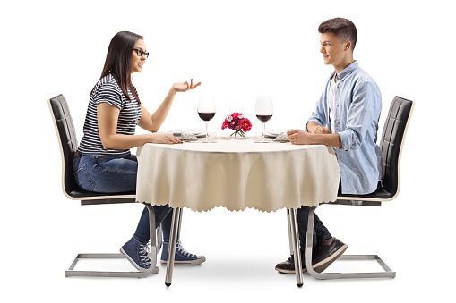 Male and female teenagers sitting at a restaurant table and talking isolated on white background