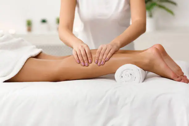 Massage therapist massaging woman calves in spa center, side view