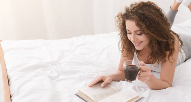 istock Cheerful girl reading book and drinking coffee in bed 1135508818