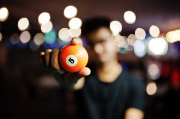 Orange pool ball with 5 hold at hands man. Blured background. Billiard theme.