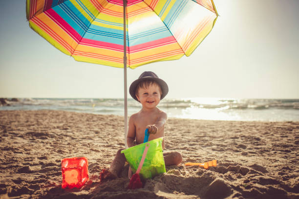 petit garçon s'asseyant sur la plage et construisant un château de sable - parasol pine photos et images de collection