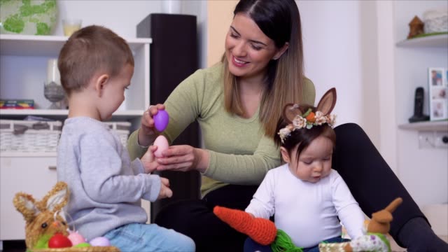 Mother with kids sitting on the floor and playing with Easter egg