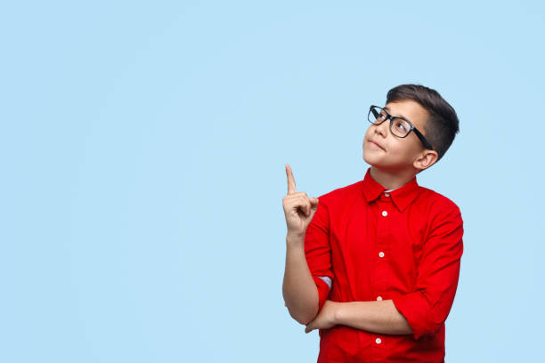 Clever boy pointing up Cute boy in red shirt and stylish glasses pointing up while standing on blue background nerd kid stock pictures, royalty-free photos & images