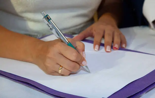detail of the hands of the bride when she signs the marriage certificate, holding a pen and wearing her wedding band and her manicure