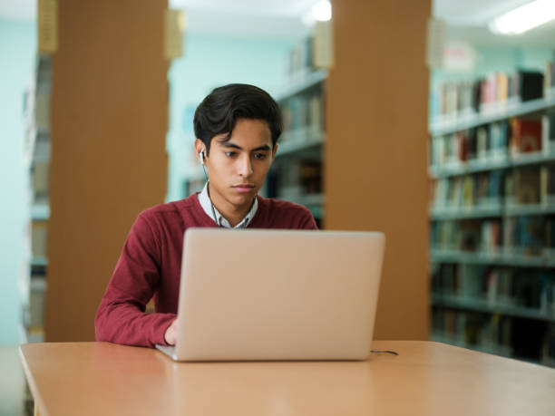 istock Young man with earphones in library 1135517371
